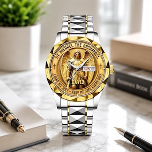 Peut inclure: Une montre-bracelet argentée et dorée présentant une image centrale en relief de Saint Michel Archange. Le cadran inclut le texte ST. MICHAEL THE ARCHANGEL, LIGHT MY WAY - KEEP ME SAFE EVERY DAY, et DAVID, avec un guichet jour-date affichant SUN 8.