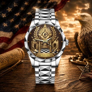 May include: A silver-toned wristwatch with a metallic link band and a faceted bezel. The brown watch face features a gold-colored Masonic square and compass emblem, an all-seeing eye, a checkered floor pattern, and the name KEVIN printed in gold.