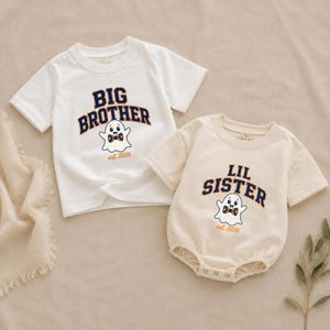May include: A white short-sleeved t-shirt with the text BIG BROTHER and a cream-colored short-sleeved bodysuit with the text LIL SISTER. Both garments feature a ghost graphic wearing a plaid bowtie and the text est. 2026 in dark blue and orange.