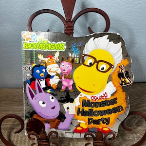May include: A children's board book titled The Backyardigans Monster Halloween Party featuring colorful cartoon characters in a laboratory setting, including a yellow character in a lab coat, a purple creature, a mummy, and a vampire penguin.