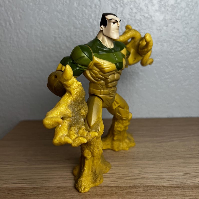 Puede incluir: Una figura de acci&oacute;n de pl&aacute;stico de un personaje musculoso con una expresi&oacute;n severa. La figura es principalmente amarilla y verde, con ap&eacute;ndices texturizados en forma de garra. La figura est&aacute; posada en una postura din&aacute;mica, sugiriendo acci&oacute;n.