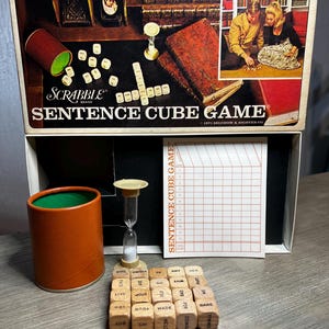 May include: Vintage Scrabble Sentence Cube Game box set. The box features the game title and a picture of people playing. Includes wooden dice with words, a timer, a score sheet, and a cup.