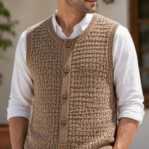 May include: A tan sleeveless knit vest featuring a textured grid pattern, a round neckline, and a front button placket with five square wooden buttons. The garment is worn over a crisp white long-sleeved shirt with a classic collar and cuffs.
