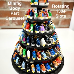 Puede incluir: Un soporte giratorio negro de varios niveles para torsos de minifiguras, con el texto Minifig Body Part Carousel, Rotating 130+ Slots y RAPID BRICKS. El soporte sostiene numerosos torsos de minifiguras de plástico de colores variados.