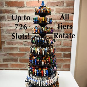May include: A black, multi-tiered, rotating display stand for small plastic figures, shaped like a cone. The stand features numerous circular levels filled with various colorful minifigures. Text on the image reads: Up to 726 Slots! All Tiers Rotate.