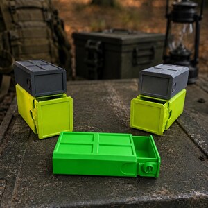 Pu&ograve; includere: Tre contenitori rettangolari con cassetti scorrevoli. Due contenitori sono impilati con coperchi grigio scuro e basi verde lime brillante. Un contenitore &egrave; posizionato in piano in primo piano, con un esterno verde lime e una manopola laterale.