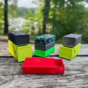 Pu&ograve; includere: Una collezione di contenitori rettangolari con cassetti scorrevoli. Il set include un contenitore rosso, due contenitori verde lime con coperchi grigio scuro e una pila di tre contenitori in nero, grigio e con motivo mimetico blu e nero.