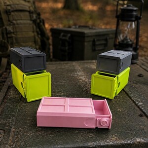 Pu&ograve; includere: Tre contenitori rettangolari con cassetti scorrevoli. Due unit&agrave; sono impilate con coperchi grigio scuro e basi verde lime. Un'unit&agrave; &egrave; posizionata orizzontalmente in primo piano, caratterizzata da un esterno rosa chiaro e una manopola laterale.