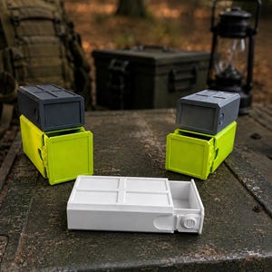 Pu&ograve; includere: Due contenitori rettangolari con cassetti scorrevoli verde lime e gusci esterni grigio scuro, posizionati in verticale. Un terzo contenitore bianco abbinato &egrave; appoggiato orizzontalmente in primo piano con un design a cassetto.