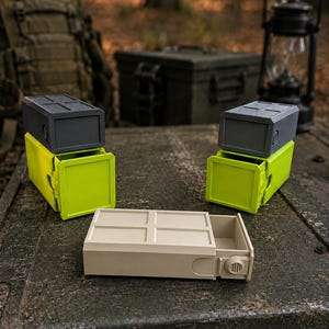 Pu&ograve; includere: Tre contenitori rettangolari con cassetti scorrevoli. Due contenitori presentano una base verde lime con un coperchio grigio scuro, mentre il terzo &egrave; di colore beige. Ogni unit&agrave; ha una parte superiore con motivo a griglia e una piccola manopola.