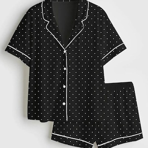 May include: Black pajama set with white polka dots. The short-sleeved top has a notched collar and button-down front. The shorts have an elastic waistband. Both pieces are trimmed with white piping.