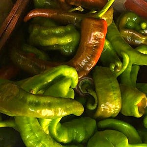 May include: A close-up shot of a collection of fresh, vibrant green and red-orange peppers. The peppers are of varying shapes and sizes, with some curved and others straight. The colors range from bright green to a deep red-orange, suggesting different stages of ripeness.