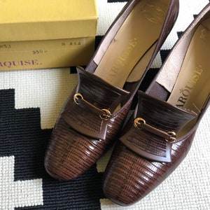 May include: A pair of brown leather heeled shoes with gold buckles. The shoes have a textured pattern and the brand name "Marquise" is printed on the box.