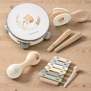 Può includere: Una collezione di strumenti musicali in legno per bambini, tra cui un tamburello, nacchere, una maraca, uno xilofono e bacchette. Ogni strumento presenta un'illustrazione di scoiattolo e colori pastello tenui. Il tamburello è etichettato "Tambourine".