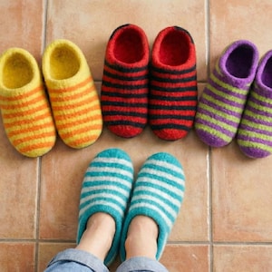 Może przedstawiać: Kolekcja kolorowych, pasiastych filcowych kapci. Kapcie są w różnych kolorach, w tym żółtym i pomarańczowym, czerwonym i czarnym, fioletowym i zielonym oraz niebieskim i białym. Kapcie są ułożone na kafelkowej podłodze.