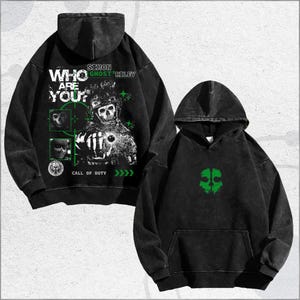 Puede incluir: Dos sudaderas con capucha negras con un aspecto desgastado. Una presenta un gráfico de un soldado calavera con el texto "WHO ARE YOU?" y "CALL OF DUTY". La otra tiene un diseño de calavera verde. Ambas tienen capucha y bolsillo delantero.