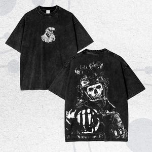 Könnte beinhalten: Zwei schwarze T-Shirts mit einem Used-Look. Eines zeigt eine Totenkopf-Grafik mit dem Wort "Ghost", das andere ein Soldaten-Totenkopf-Design. Beide haben kurze Ärmel und einen Rundhalsausschnitt.