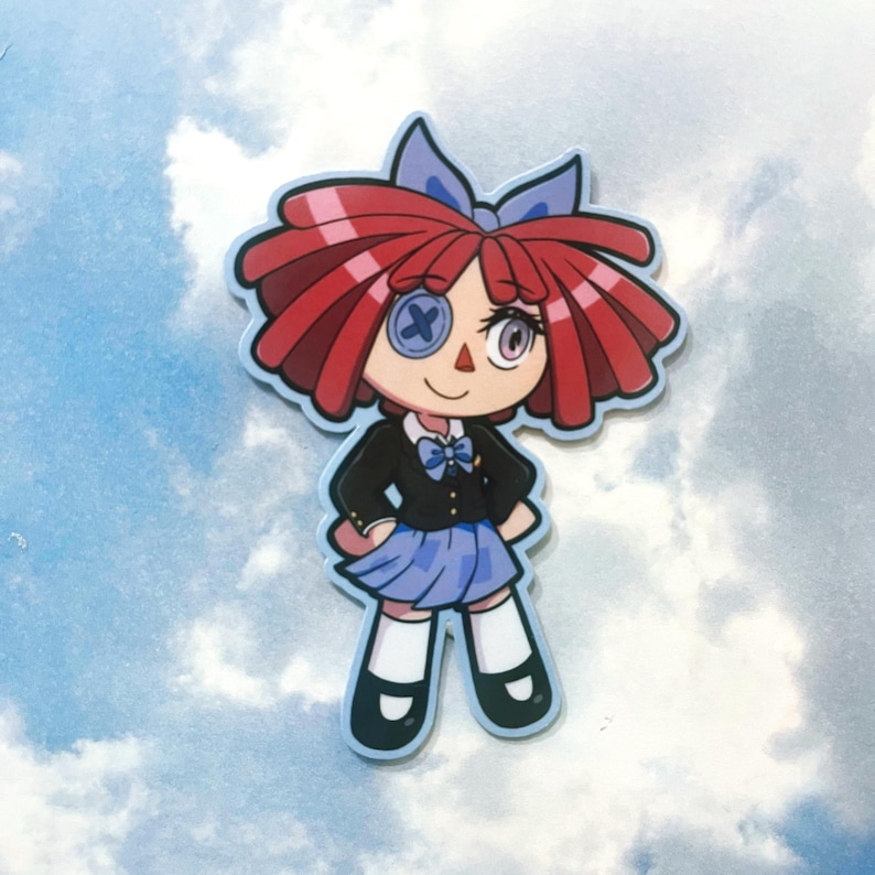 Op de afbeelding: Een sticker met een cartoonpop met rood haar, een blauwe strik en een zwart jasje over een blauwe rok. De pop heeft een knoogje als oog en lacht. De sticker heeft een lichtblauwe rand en een hemelachtergrond.