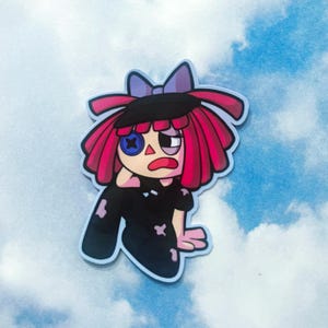 Op de afbeelding: Een sticker met een cartoonpop met rood haar, een zwarte hoed en een paarse strik. De pop heeft een knoopoog en een gestikte mond. De pop draagt een zwarte outfit met patches.