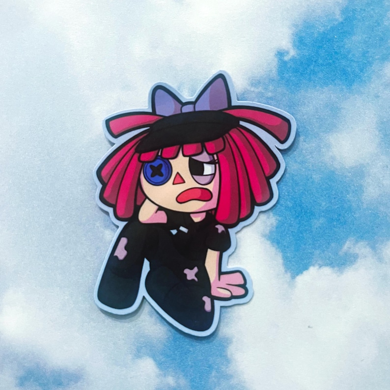 Op de afbeelding: Een sticker met een cartoonpop met rood haar, een zwarte hoed en een paarse strik. De pop heeft een knoopoog en een gestikte mond. De pop draagt een zwarte outfit met patches.
