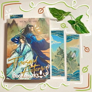 Puede incluir: Un conjunto de libro y marcapáginas. La portada del libro presenta dos figuras con túnicas fluidas sobre un paisaje. El título "Thousand Autumns" es visible. Dos marcapáginas representan una escena de montaña y un rollo.
