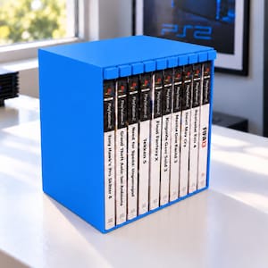 May include: A bright blue plastic storage rack holding ten PlayStation 2 video game cases. The spines are visible, displaying titles including Tony Hawk's Pro Skater 4, Grand Theft Auto: San Andreas, Need for Speed: Underground, Tekken 5, Final Fantasy X, Kingdom Hearts II, Metal Gear Solid 3, Devil May Cry, Resident Evil 4, and FIFA 13.