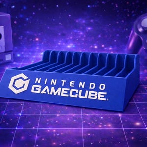 Peut inclure: Un support bleu pour cartouches de jeux Nintendo GameCube avec le logo et le texte GameCube. Le support comporte plusieurs fentes pour les cartouches de jeux. Une console, une manette et une carte mémoire GameCube sont en arrière-plan.