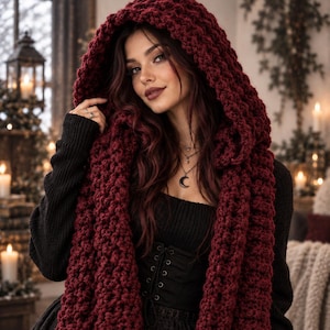 May include: A deep burgundy chunky knit hooded scarf featuring a thick, textured yarn construction. The long, wide scarf drapes over the shoulders and includes an integrated hood, providing full coverage for the head and neck in a dark red hue.