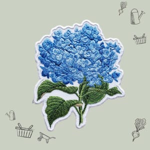 May include: Embroidered patch featuring a vibrant blue hydrangea flower with green leaves and a white border. The patch showcases detailed stitching, capturing the texture of the petals and foliage. The design is set against a light gray background with gardening-themed illustrations.