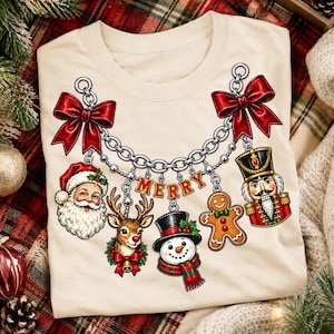 Puede incluir: Una camiseta de color crema con un gráfico de un collar de cadena plateada con dos grandes lazos rojos. De la cadena cuelgan dijes de Santa Claus, un reno, un muñeco de nieve, un hombre de jengibre, un cascanueces y la palabra MERRY en rojo.