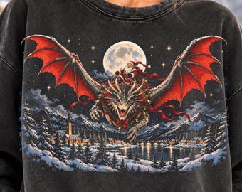 May include: A charcoal grey crewneck sweatshirt featuring a graphic print of Santa Claus riding a large dragon with expansive red wings. The scene includes a full moon, a starry night sky, and a snow-covered village with mountains in the background.