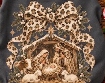 May include: A dark gray sweatshirt featuring a graphic of a nativity scene with a large leopard print bow above it. The design includes figures in leopard print clothing, a cow, two lambs, and pine branches with white berries.