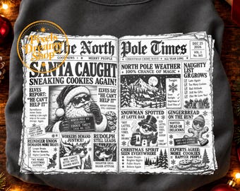 May include: A dark gray sweatshirt featuring a graphic print of a newspaper titled The North Pole Times. The design includes headlines about Santa caught stealing cookies, a snowman, a gingerbread person, and reindeer, all in black and white.