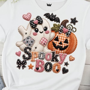 Puede incluir: Una camiseta blanca con un diseño gráfico de un fantasma con un lazo de lunares negros, una calabaza a cuadros naranjas, un murciélago negro y varios corazones y estrellas. El texto "Spooky Boo" aparece en una fuente estampada bajo las figuras.
