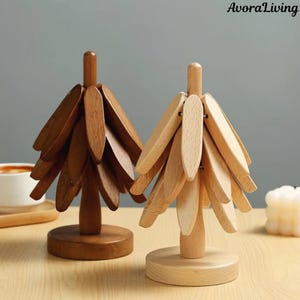 May include: Two wooden decorative trees. One is a dark brown colour, and the other is a light natural wood colour. Each tree has a round base and a series of wooden leaf-shaped pieces attached to a central wooden pole.