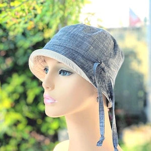 May include: A denim-style cloche hat with a white brim and matching ties. The hat is a light blue color and has a soft, textured appearance. The ties are knotted at the ends.