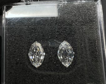 Puede incluir: Dos diamantes incoloros de talla marquesa presentados dentro de un estuche de almacenamiento cuadrado de plástico transparente con acolchado de espuma negra. Los diamantes tienen una superficie facetada que refleja la luz.