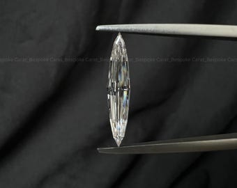 Puede incluir: Una piedra preciosa suelta con talla marquesa, de aspecto transparente, incoloro y altamente facetado. La piedra se sostiene verticalmente con unas pinzas metálicas, mostrando su forma alargada y puntiaguda junto a sus reflejos de luz.