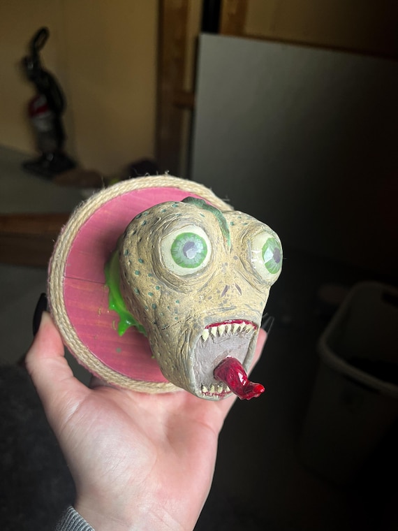 A one-of-a-kind wall-hanging creature sculpture — weird, tongue-out, gothic, and unmistakably handmade, the kind of thing guests will immediately ask about.
