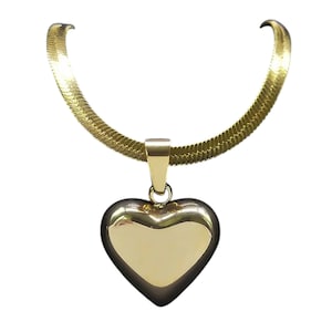 Op de afbeelding: Een goudkleurige ketting met een hartvormige hanger. De hanger is een massief, gepolijst hart. De ketting heeft een textuur, slangachtig ontwerp. De sieraden staan tegen een witte achtergrond.