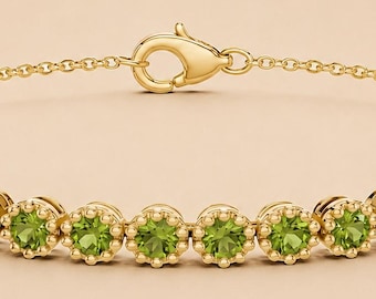 May include: A gold chain bracelet featuring a series of round, vibrant green peridot gemstones, each set in a scalloped gold bezel. The bracelet includes a lobster claw clasp and is positioned above the text LyraJewelryGift on a light background.