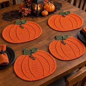 May include: Three orange pumpkin-shaped crochet placemats with green stems and curly vines. Each placemat features a textured, circular stitch pattern mimicking the ridges of a pumpkin, designed to lay flat on a dining surface for seasonal decor.