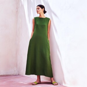 May include: A sleeveless olive green maxi dress featuring a round neckline and a loose, flowing silhouette that reaches the ankles. The garment includes side pockets and is paired with matching olive green flat slide sandals.