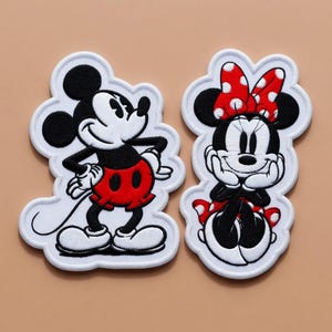 May include: Embroidered patches featuring Mickey Mouse and Minnie Mouse. Mickey is in a standing pose with red shorts. Minnie is seated, wearing a red bow with white polka dots and a red and white polka dot skirt. Both have white outlines.