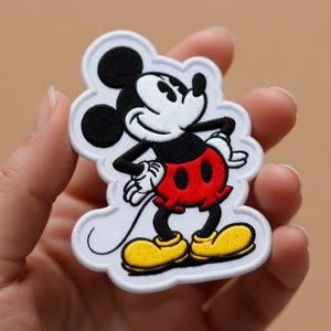May include: Embroidered patch featuring Mickey Mouse in a classic pose. The patch has a white border, black ears, a white face, red shorts, yellow shoes, and black arms and legs. A fun, colorful accessory for clothing or bags.