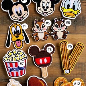 May include: Embroidered patches featuring Disney characters and park-themed food items. Includes Mickey Mouse, Minnie Mouse, Donald Duck, Pluto, Chip and Dale, popcorn, ice cream, a Mickey ice cream bar, a turkey leg, and a Mickey pretzel.
