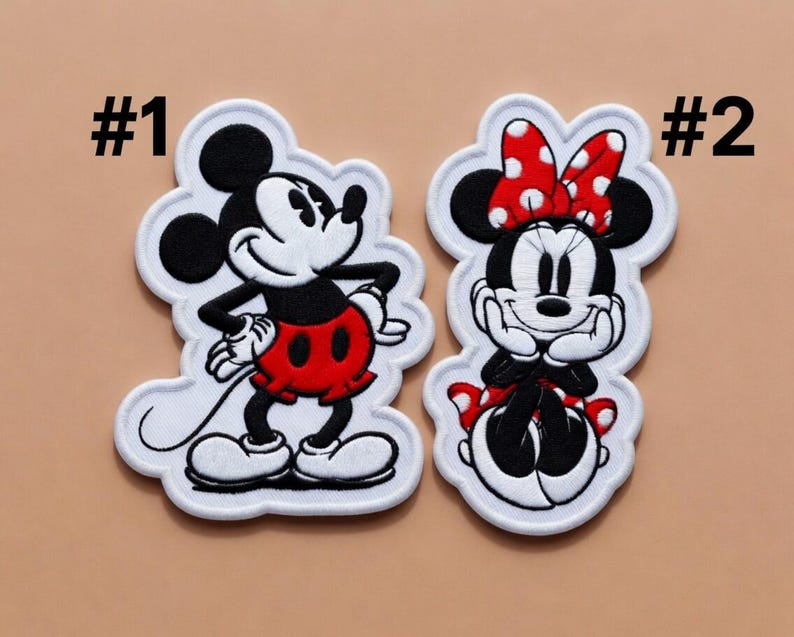 May include: Two embroidered patches featuring cartoon characters. One patch depicts Mickey Mouse in black, white, and red, with the number "#1" above it. The second patch shows Minnie Mouse in black, white, and red, with a red polka dot bow and the number "#2" above it.