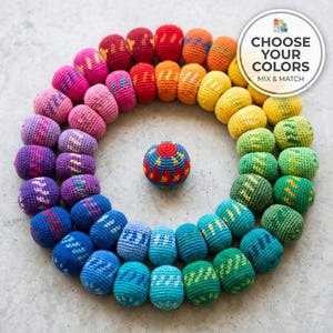 Puede incluir: Una vibrante exhibición de pelotas de malabares de ganchillo dispuestas en un patrón circular, mostrando un espectro de colores del rojo al azul. Una bola central presenta un patrón detallado. La imagen incluye el texto "CHOOSE YOUR COLORS MIX & MATCH."