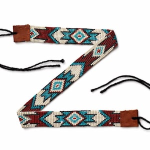 Könnte beinhalten: Ein Stirnband mit Perlenbesatz im indianischen Design. Das Stirnband hat ein Muster aus weißen, türkisfarbenen und weinroten Perlen. Die Enden sind mit braunem Leder und schwarzen Kordeln zum Binden versehen.