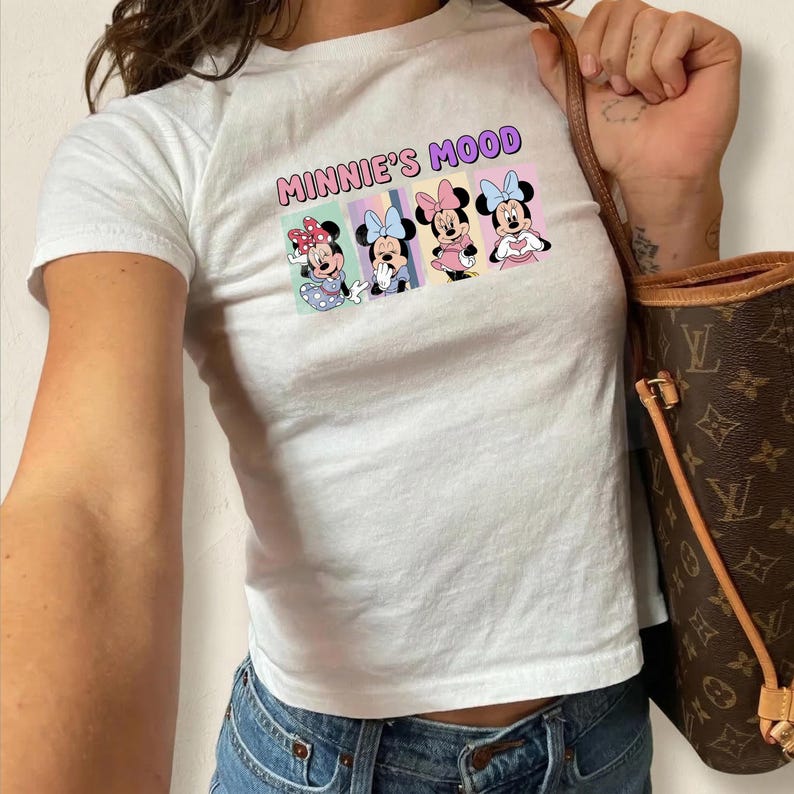 May include: White crop top featuring the text "MINNIE'S MOOD" above a graphic of Minnie Mouse in four different outfits. The graphic includes Minnie with polka dots, bows, and various colors.